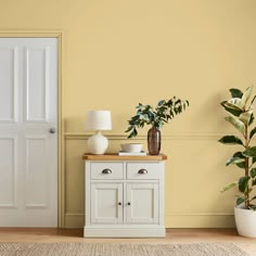 a white cabinet sitting next to a potted plant on top of a wooden table