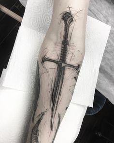 a cross tattoo on the arm with a knife in it's center and an arrow at the top