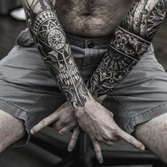 a man with tattoos on his arms sitting down and holding his hands in the air