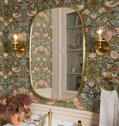 a bathroom sink under a large mirror next to a gold faucet and wall paper