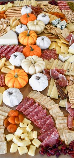 an assortment of cheeses, meats and vegetables on a platter with pumpkins