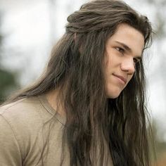 a man with long hair standing in front of a street light and looking off to the side