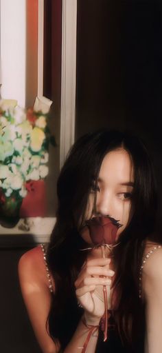 a woman holding a rose up to her face in front of a vase with flowers