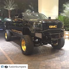 a black truck with gold rims parked in front of a large sign that says gmc