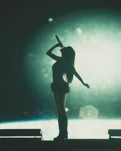 a woman standing on top of a stage with a microphone in her hand and arms behind her head