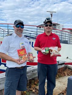 two men standing next to each other on a dock with food in front of them