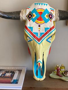 a cow's skull with colorful designs on it sitting on a table next to a book