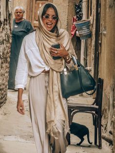 a woman is walking down the street with her purse and cell phone in hand as she smiles