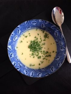 a blue and white bowl filled with soup on top of a black table next to a spoon