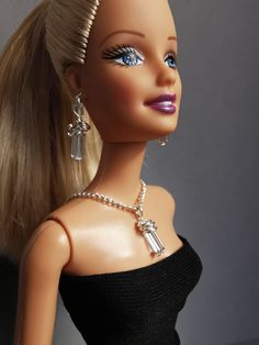 a barbie doll with blonde hair and blue eyes wearing a black dress, necklace and earrings