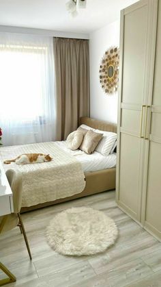 a cat laying on top of a bed next to a white desk and chair in a bedroom