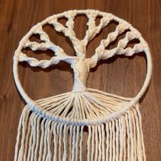 a white crocheted tree of life hanging from a wooden table with wood flooring