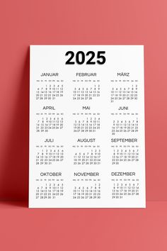 a white calendar with the year in black on a pink background, next to a red wall