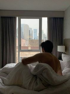 a man is laying in bed with his back turned to the camera and looking out an open window