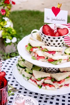 a stack of sandwiches sitting on top of a white plate next to a cup filled with strawberries