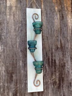 three green glass pots hanging on a wooden wall