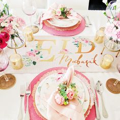 the table is set with pink flowers and gold place settings