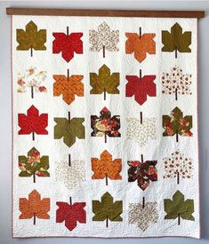 a quilted wall hanging with autumn leaves on the front and back, along with an oak frame