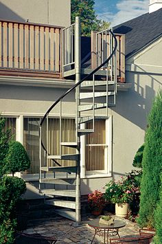 a spiral staircase in front of a house with potted plants on the patio and table