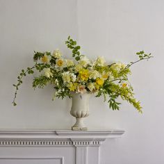 a white vase filled with yellow and white flowers on top of a fireplace mantel