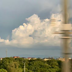 an airplane flying in the sky over some trees and buildings under a cloudy blue sky