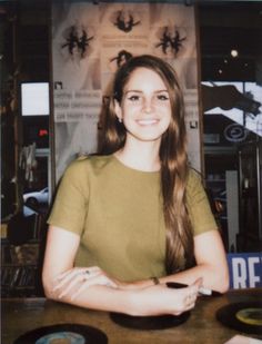 a young woman sitting at a table with her arms crossed in front of the camera