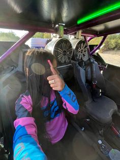 a girl in the back of a car with her hand up and pointing to the camera