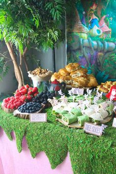 a table topped with lots of food next to a green plant covered wall and potted tree