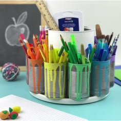 a cup filled with lots of colorful pens and pencils next to a pile of crayons