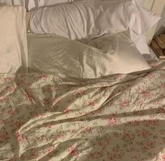 an unmade bed with white sheets and pink flowers on the comforter is shown