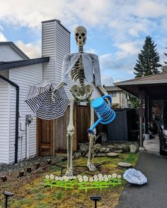 a skeleton holding an umbrella in front of a house with yard decorations on the lawn