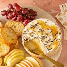 an assortment of cheeses, apples and crackers on a plate with wine glasses