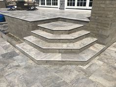 an outdoor patio with steps leading up to the front door and back porch area, surrounded by stone pavers