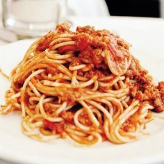 a white plate topped with spaghetti covered in sauce and ground meat next to a glass of water