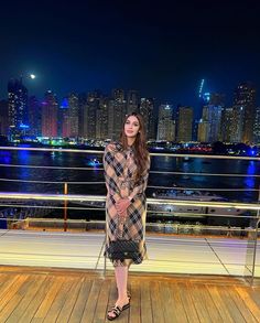 a woman standing on top of a wooden deck next to a city skyline at night