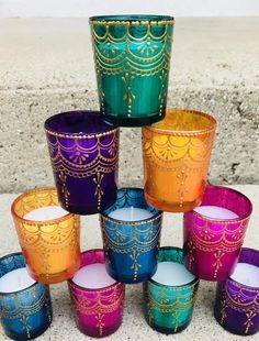 there are many different colored glass cups on the ground with one candle in front of them