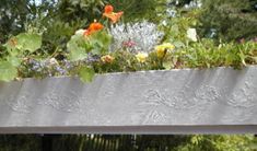 an elevated planter with flowers and plants growing on it's sides in the garden