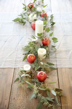 the table is set with candles, apples and greenery