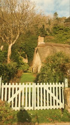 a white picket fence in front of a house with a thatched roof and trees