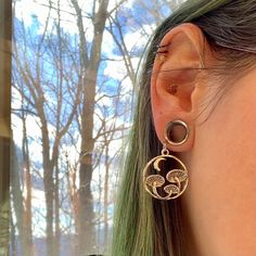 a close up of a person's ear wearing earrings with trees in the background