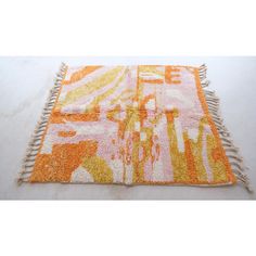 an orange and pink rug with fringes on top of white flooring next to a wall