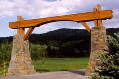 a large wooden arch in the middle of a park with trees and mountains in the background