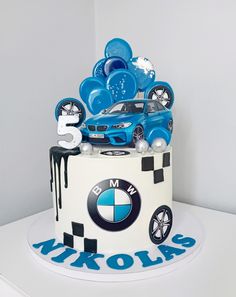 a bmw themed birthday cake with blue balloons and cars on the top, in front of a white wall