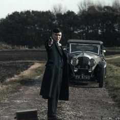 a man in a long black coat pointing at the camera