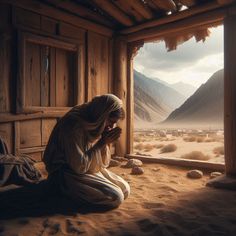 a woman kneeling down in front of a window with mountains behind her and rocks on the ground