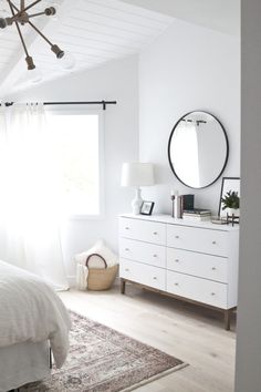 a bedroom with white furniture and a large round mirror on the wall above the bed