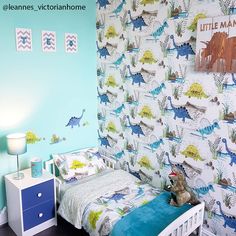 a small child's bedroom with dinosaur wallpaper and blue bedding, along with two nightstands