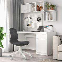 a white desk with a laptop computer on top of it next to a chair and bookshelf