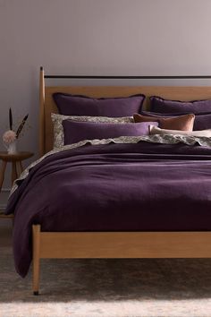 a bed with purple comforter and pillows in a gray room next to a night stand