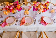 the table is set with pink and orange flowers in vases, plates, napkins, and silverware